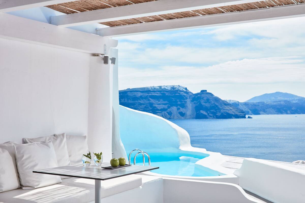 A modern, minimalist room with a pool and a view of the sea and mountains.
