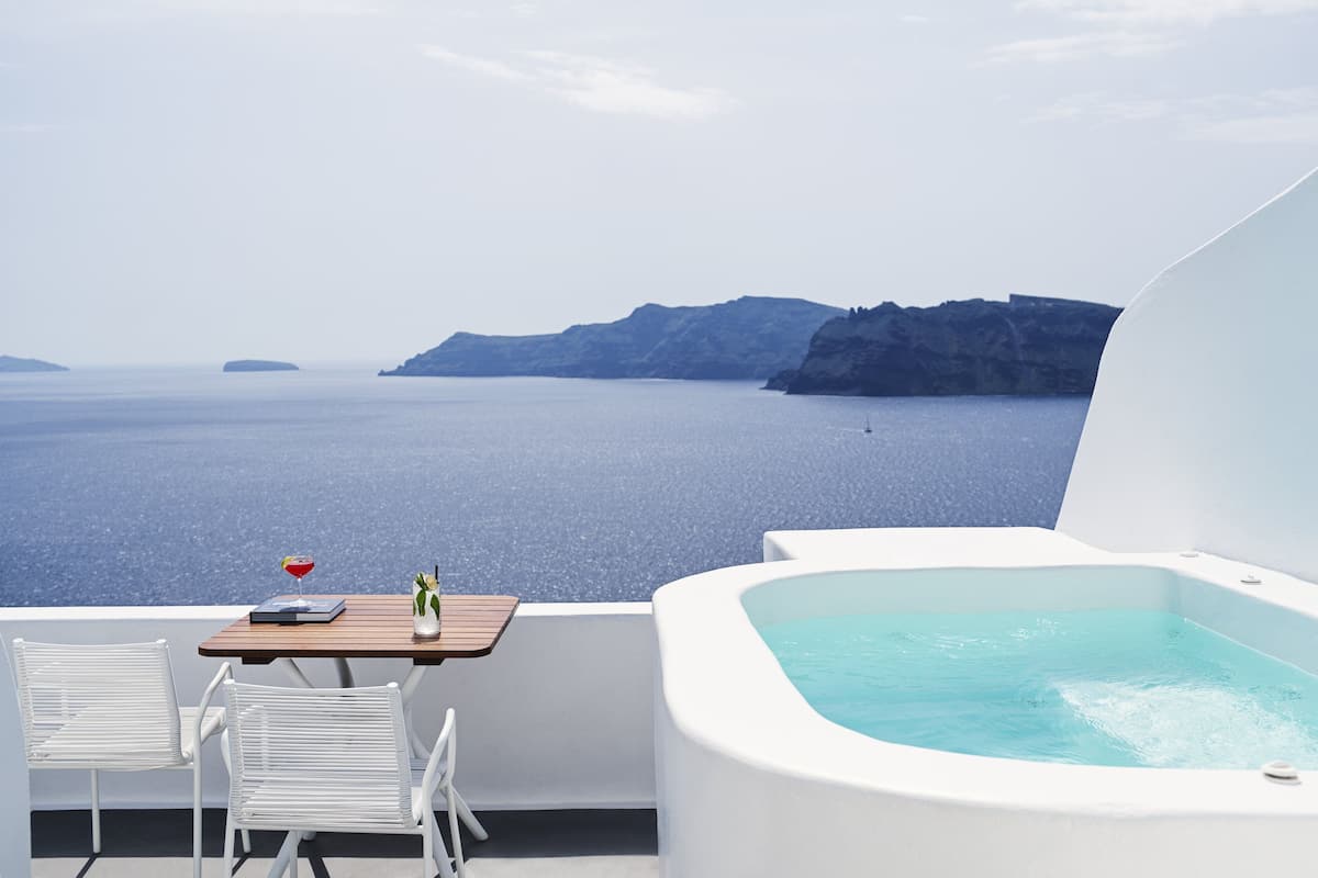 A balcony with a white hot tub and two white chairs, overlooking a large body of water and distant landforms.