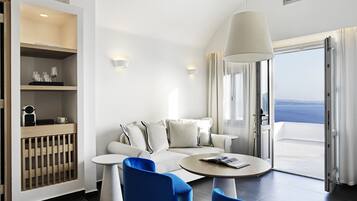 A modern room with a sofa, two chairs, a round table, and a large window offering a view of the sea.