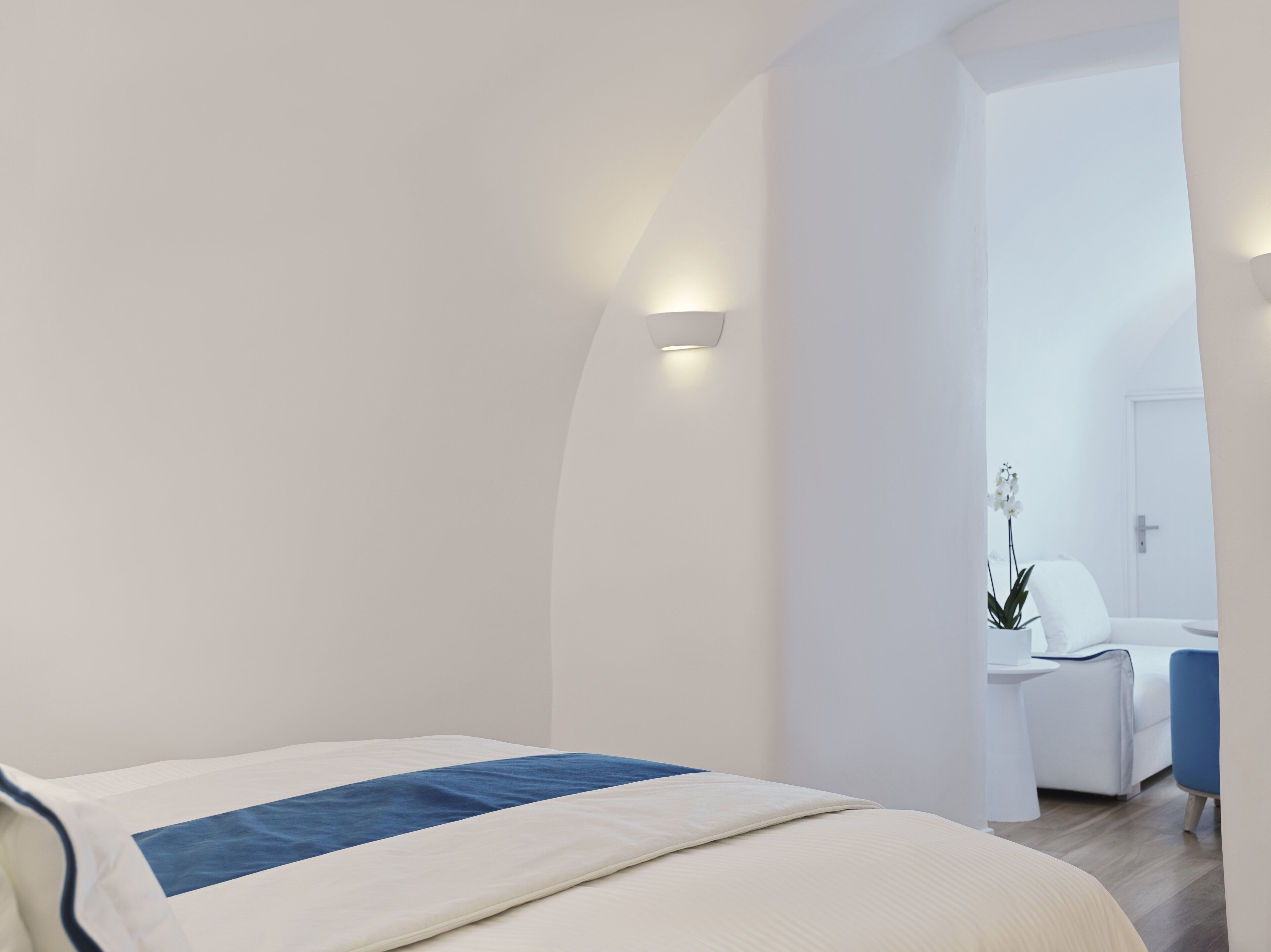 A modern bedroom with a bed, a bedside table, a chair, and a bathroom visible through an open door.