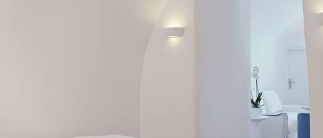 A modern bedroom with a bed, a bedside table, a chair, and a bathroom visible through an open door.