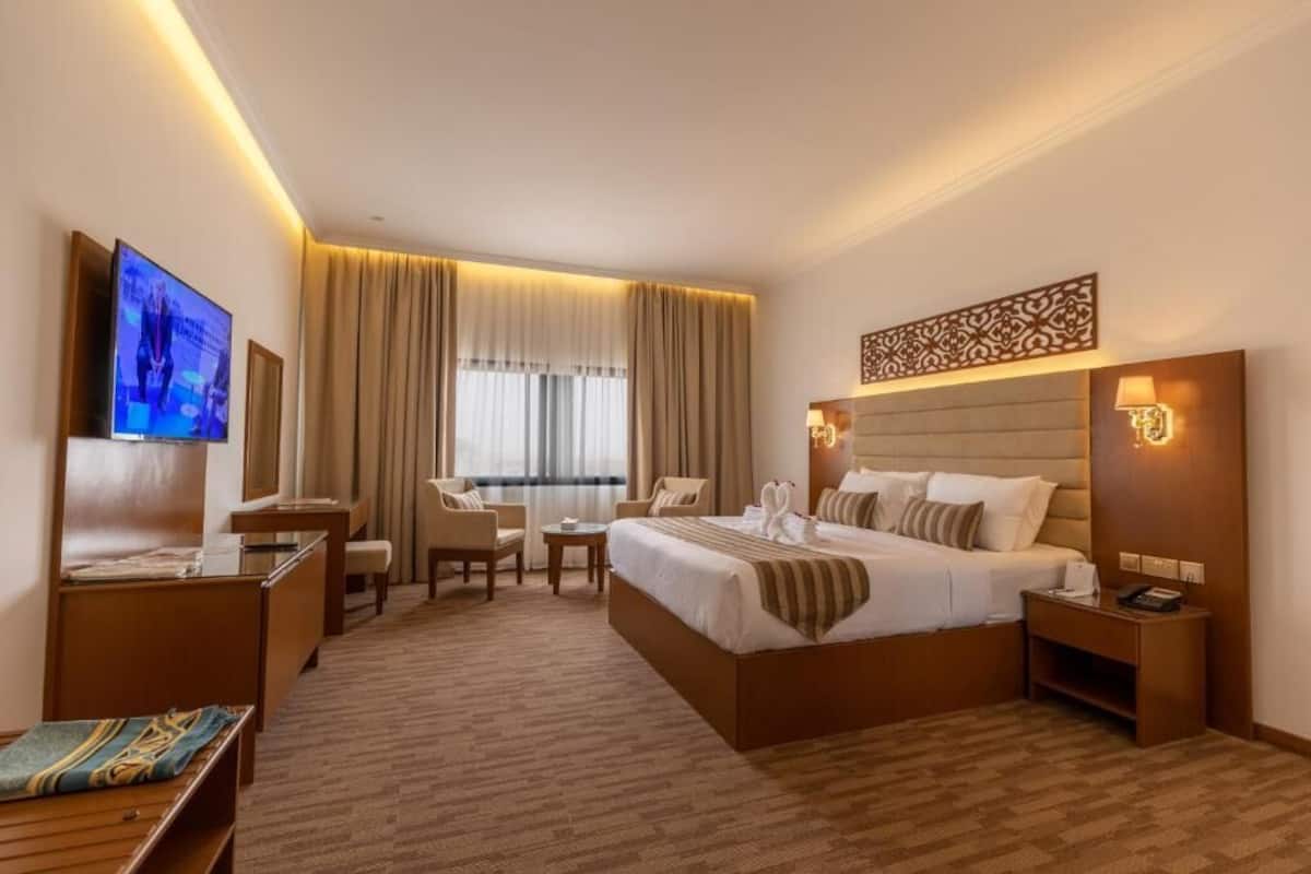 A hotel room with a large bed, a desk, a chair, a TV, and a window with curtains.