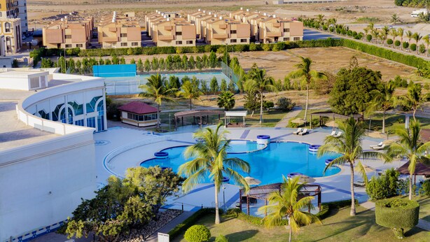 Een resort met een groot zwembad, palmbomen en een rij appartementengebouwen op de achtergrond.
