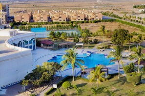 A resort with a large swimming pool, palm trees, and a row of apartment buildings in the background. - Hamdan Plaza Hotel (Salalah)