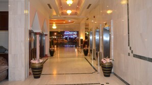 Een hotel lobby met een marmeren vloer, grote potplanten en een receptiebalie op de achtergrond.