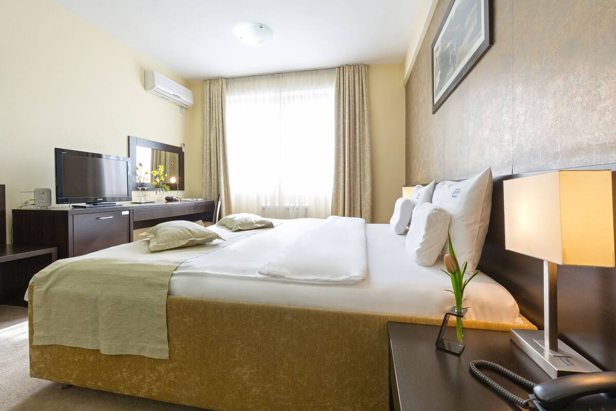 Habitación de hotel con una cama grande, un escritorio con televisor, una lámpara y un florero con flores.