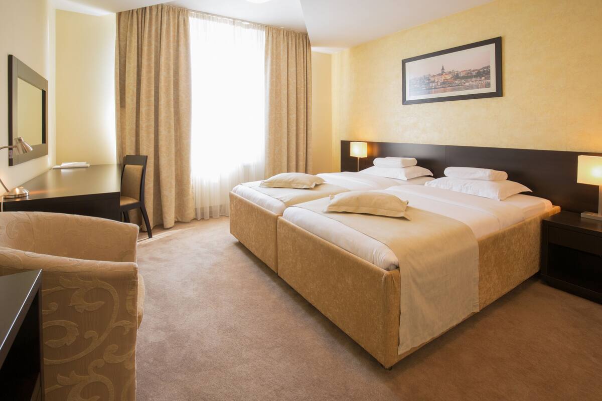 Una habitación de hotel con una cama grande, dos mesitas de noche, un escritorio y una silla.