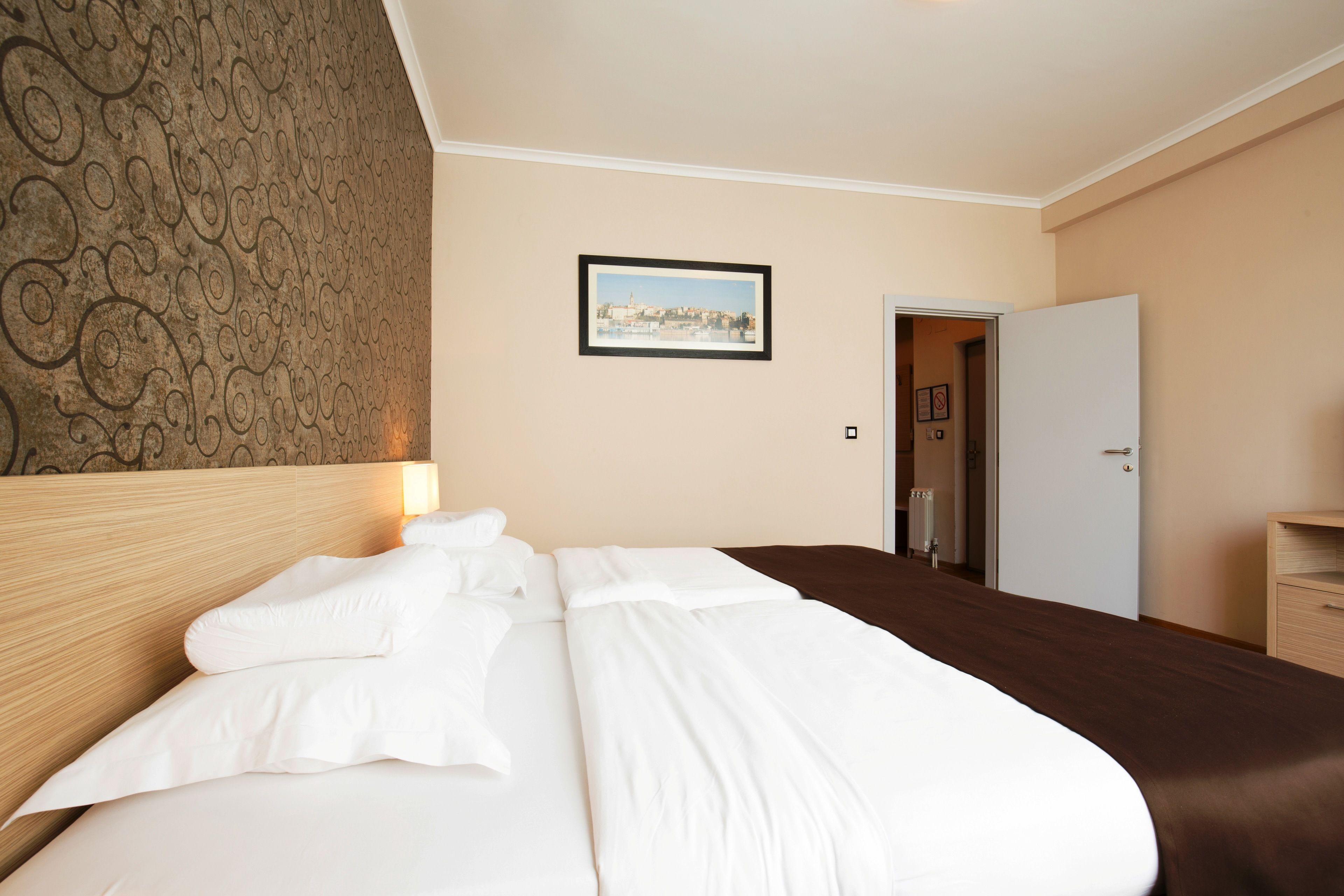 A hotel room with a neatly made bed, a framed picture on the wall, and a door leading to another room.