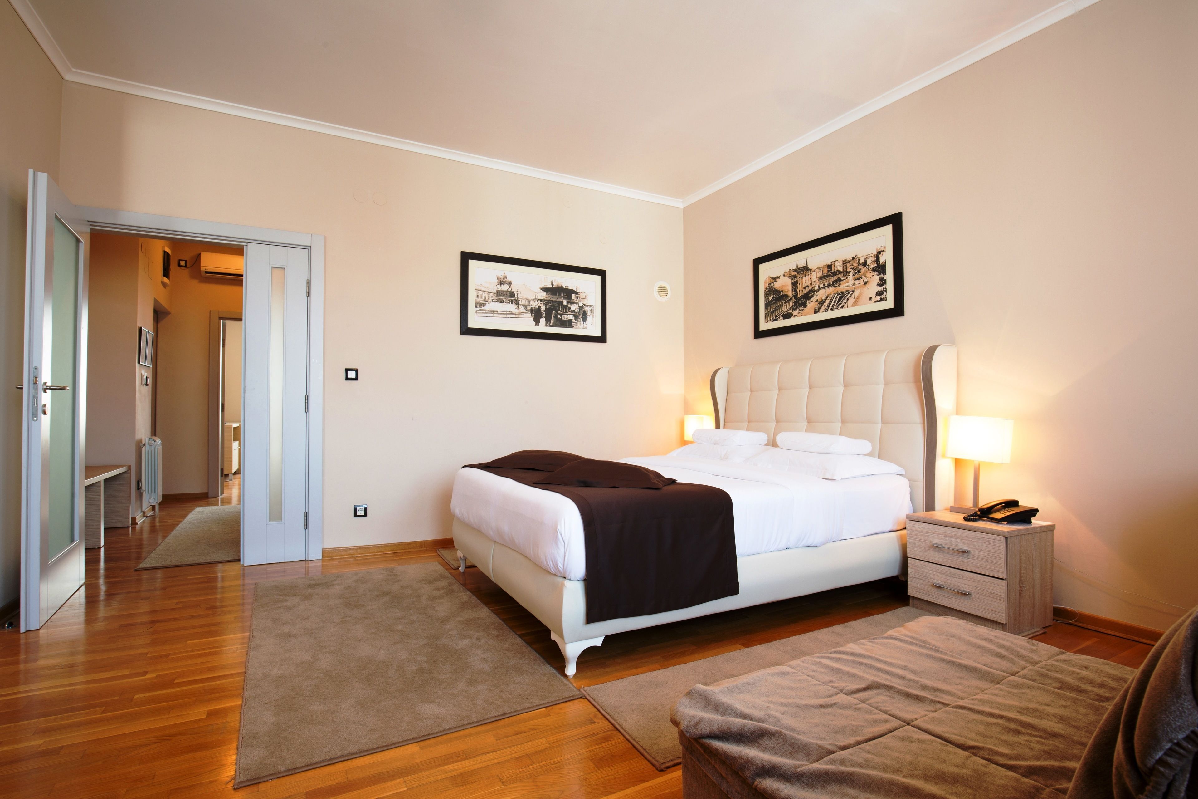 A hotel room with a bed, bedside tables, a lamp, a chair, a door, and two framed pictures on the wall.