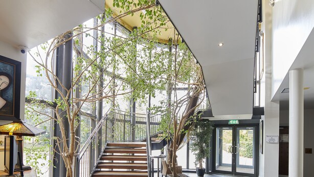 A spacious lobby with a wooden staircase, potted plants, and a modern ceiling design. - Lazaat Hotel (Cottingham)