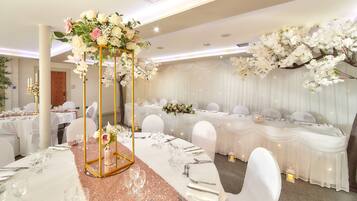 Een balzaal met ronde tafels, witte tafellakens en gouden middelpuntdecoraties.