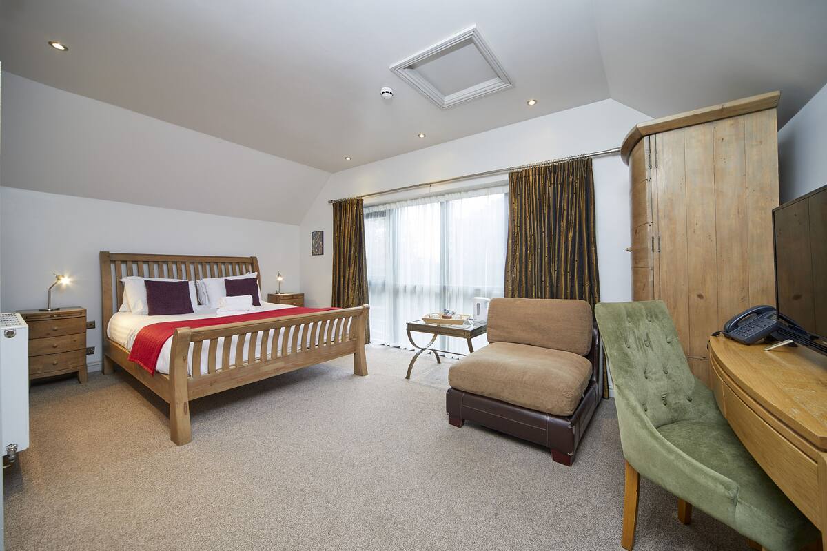 A hotel room with a wooden bed, a green armchair, a desk with a telephone, and a wardrobe.