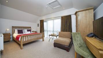 A hotel room with a wooden bed, a green armchair, a desk with a telephone, and a wardrobe.