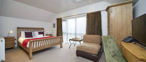 Una habitación de hotel con una cama de madera, un sillón verde, un escritorio con teléfono y un armario.