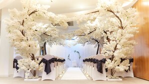A wedding aisle with white chairs and black sashes, flanked by white artificial cherry blossom trees. - Lazaat Hotel (Cottingham)