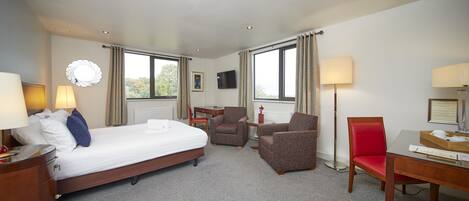 A hotel room with a bed, two armchairs, a desk, a TV, and a window with curtains.
