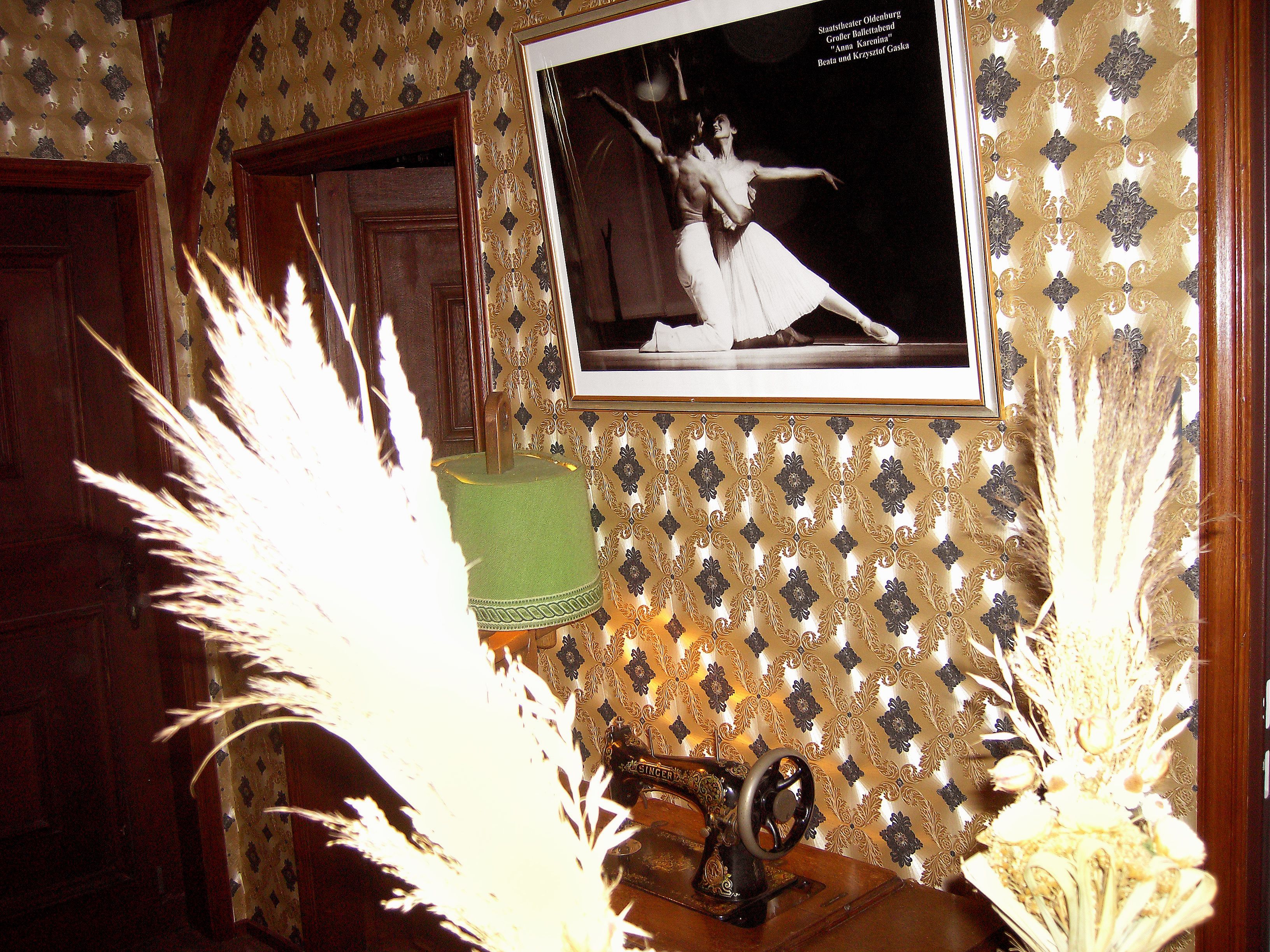 A vintage sewing machine, a framed photograph of a ballet dancer, and a patterned wallpaper.