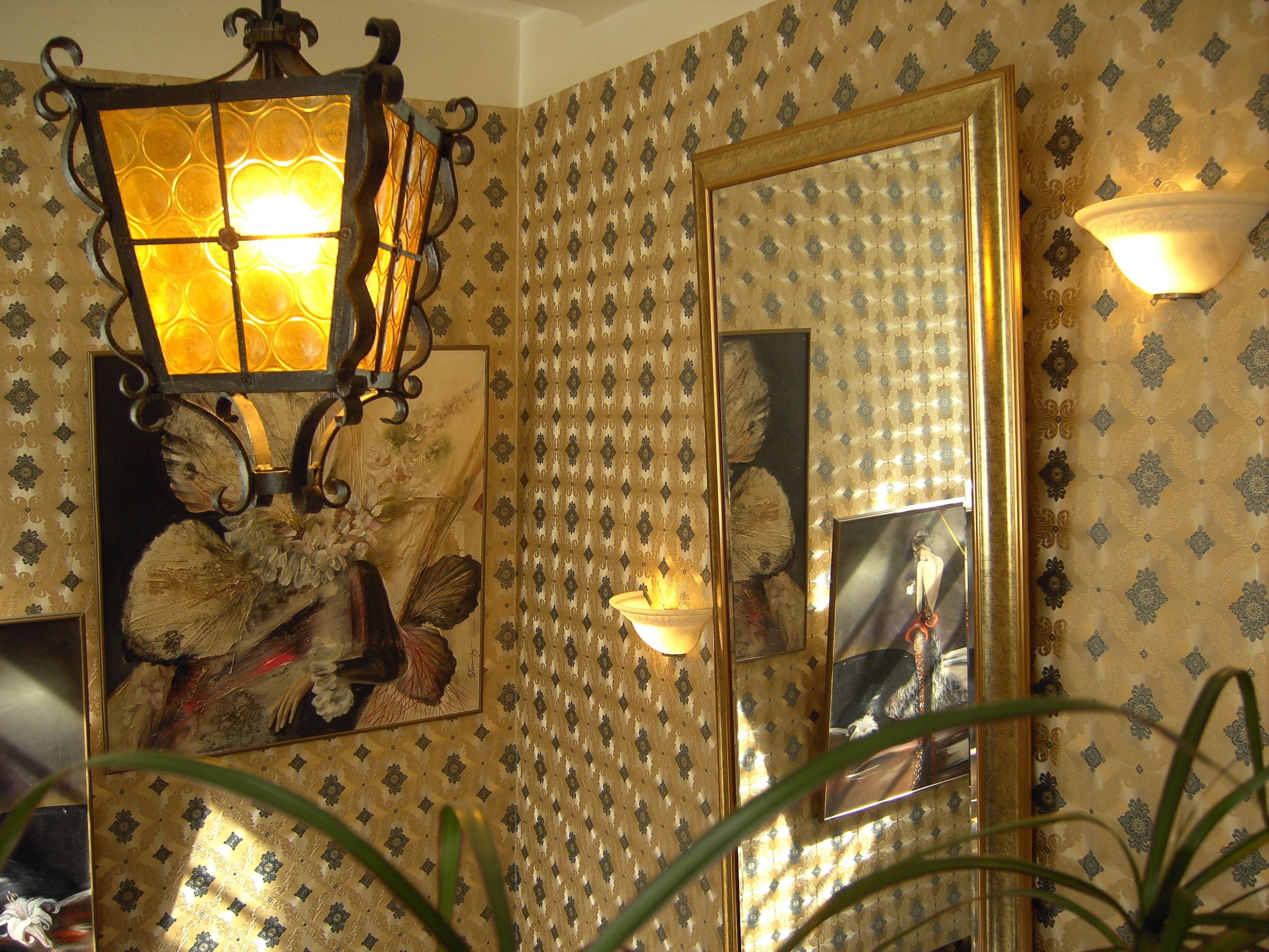 Una habitación con papel tapiz estampado, un espejo grande y una lámpara fijada a la pared.