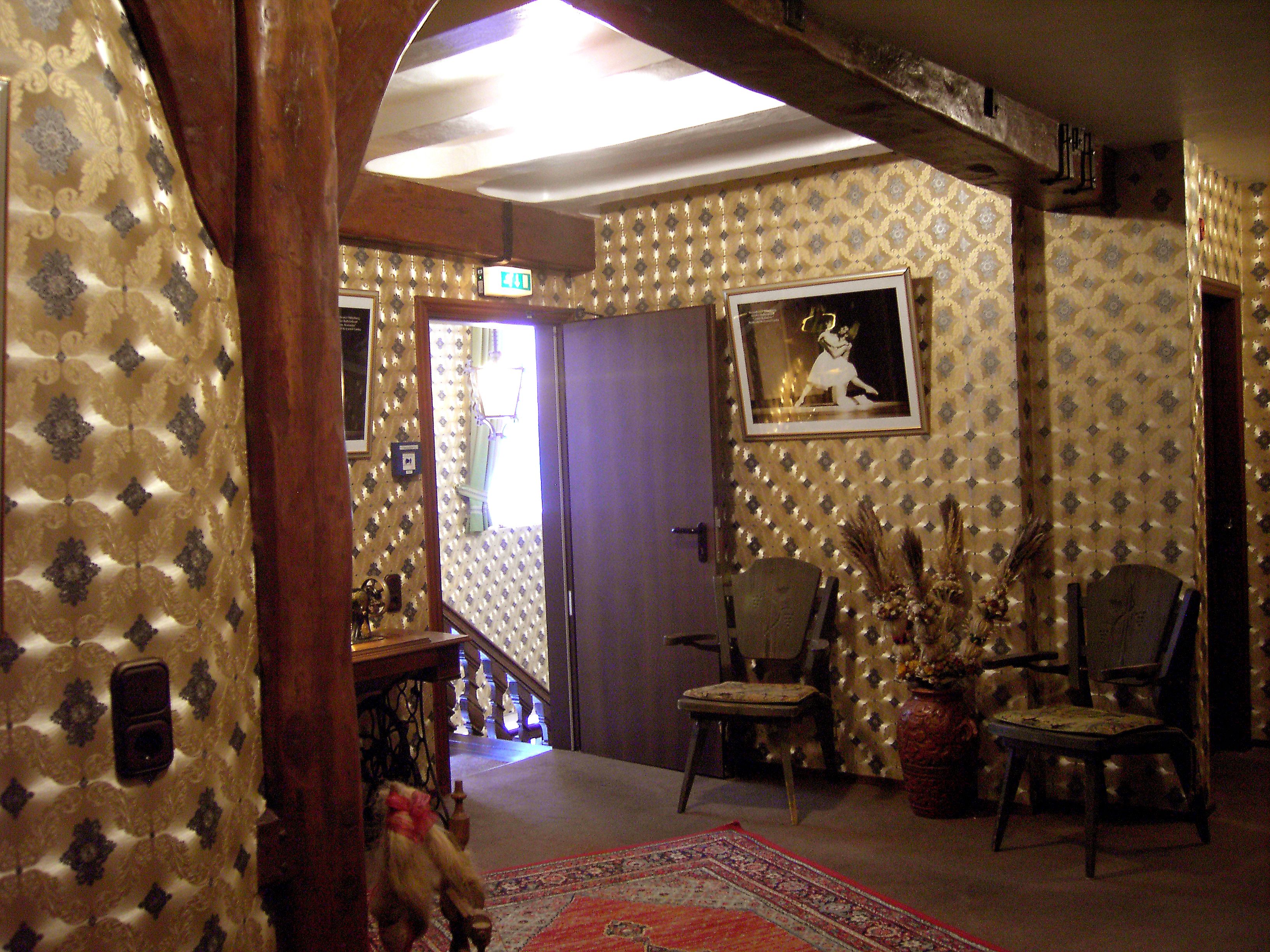 A room with patterned wallpaper, a framed picture on the wall, and several chairs.