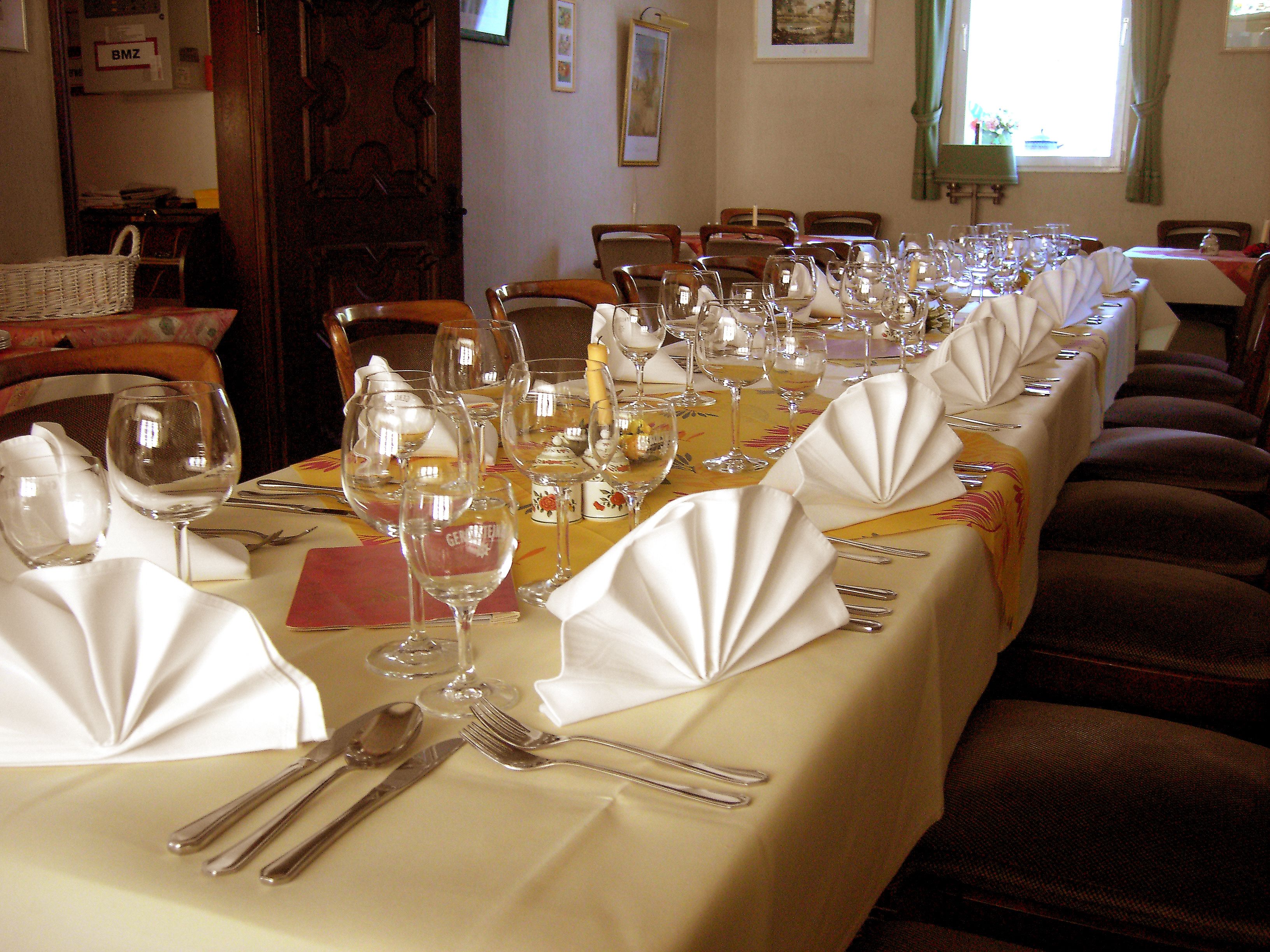 Une longue table à manger, dressée avec de nombreux verres à vin, des fourchettes et des couteaux, ce qui indique un repas formel.