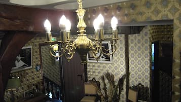 Een kamer met houten balken, traditioneel meubilair, behang met een patroon en een kroonluchter met meerdere lampen.