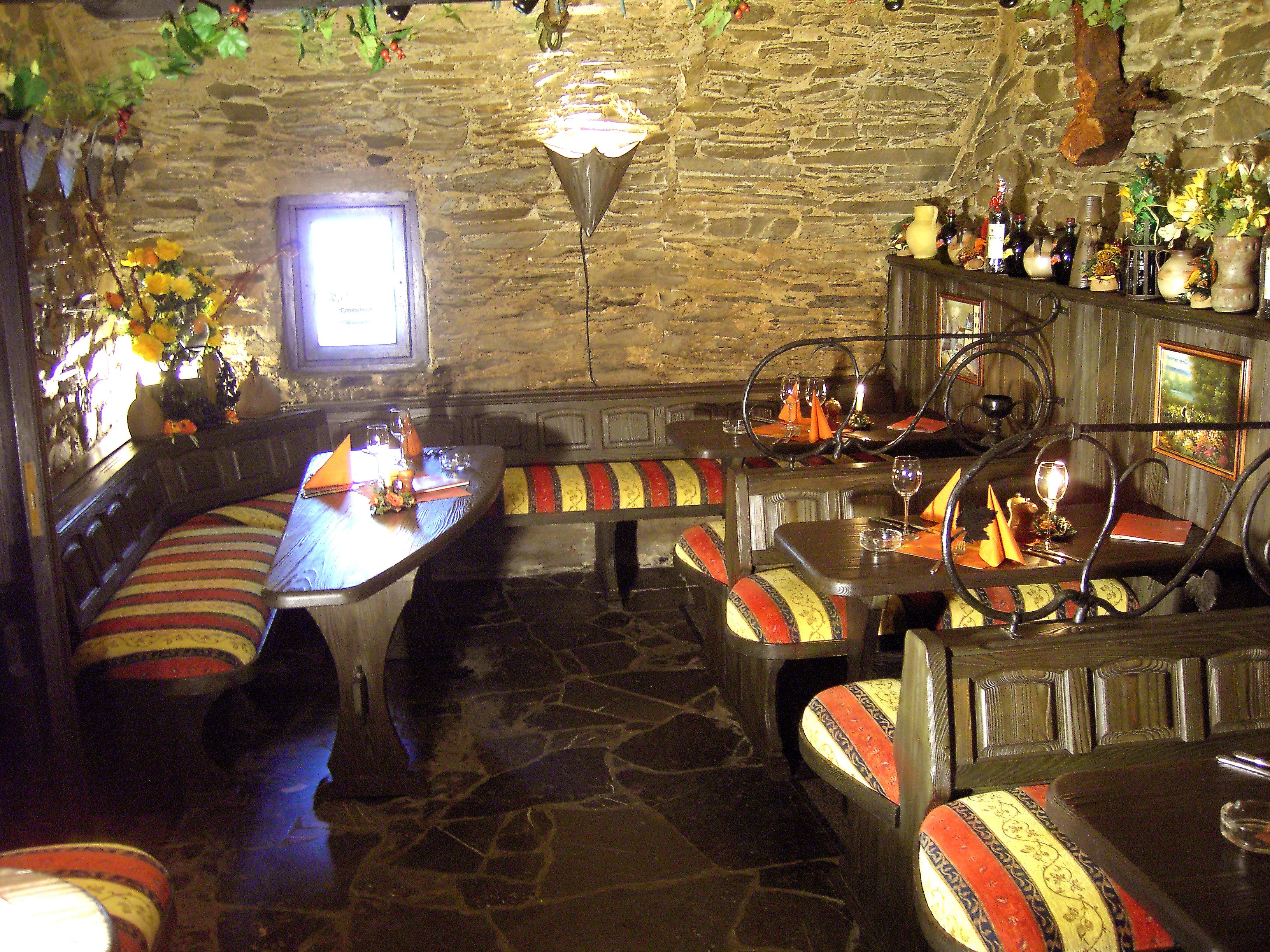 Un restaurante acogedor con paredes de piedra, muebles de madera y una variedad de botellas y flores en las estanterías.