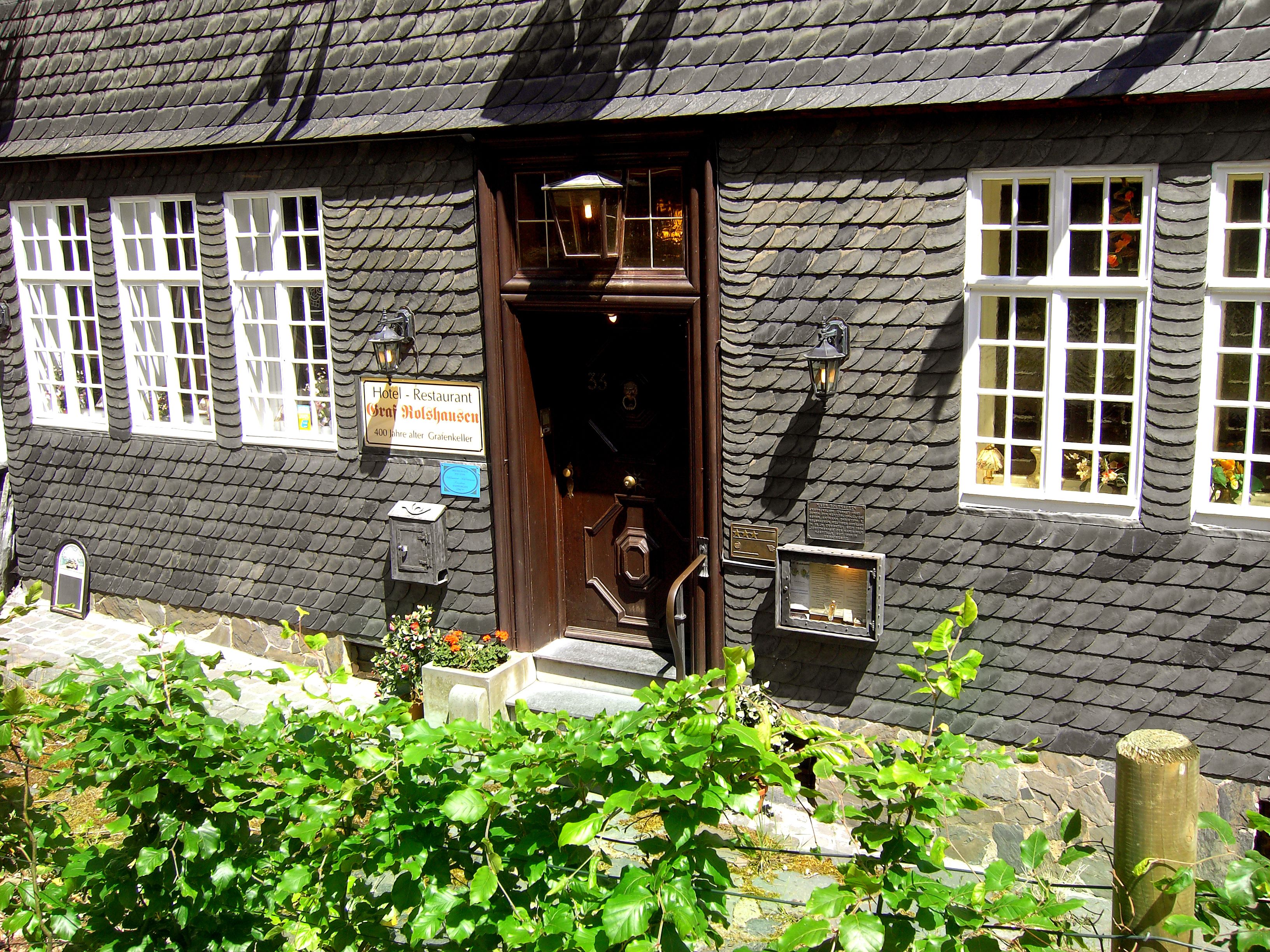 Un bâtiment traditionnel avec un toit recouvert de bardeaux sombres, une porte en bois et des fenêtres à cadre blanc.