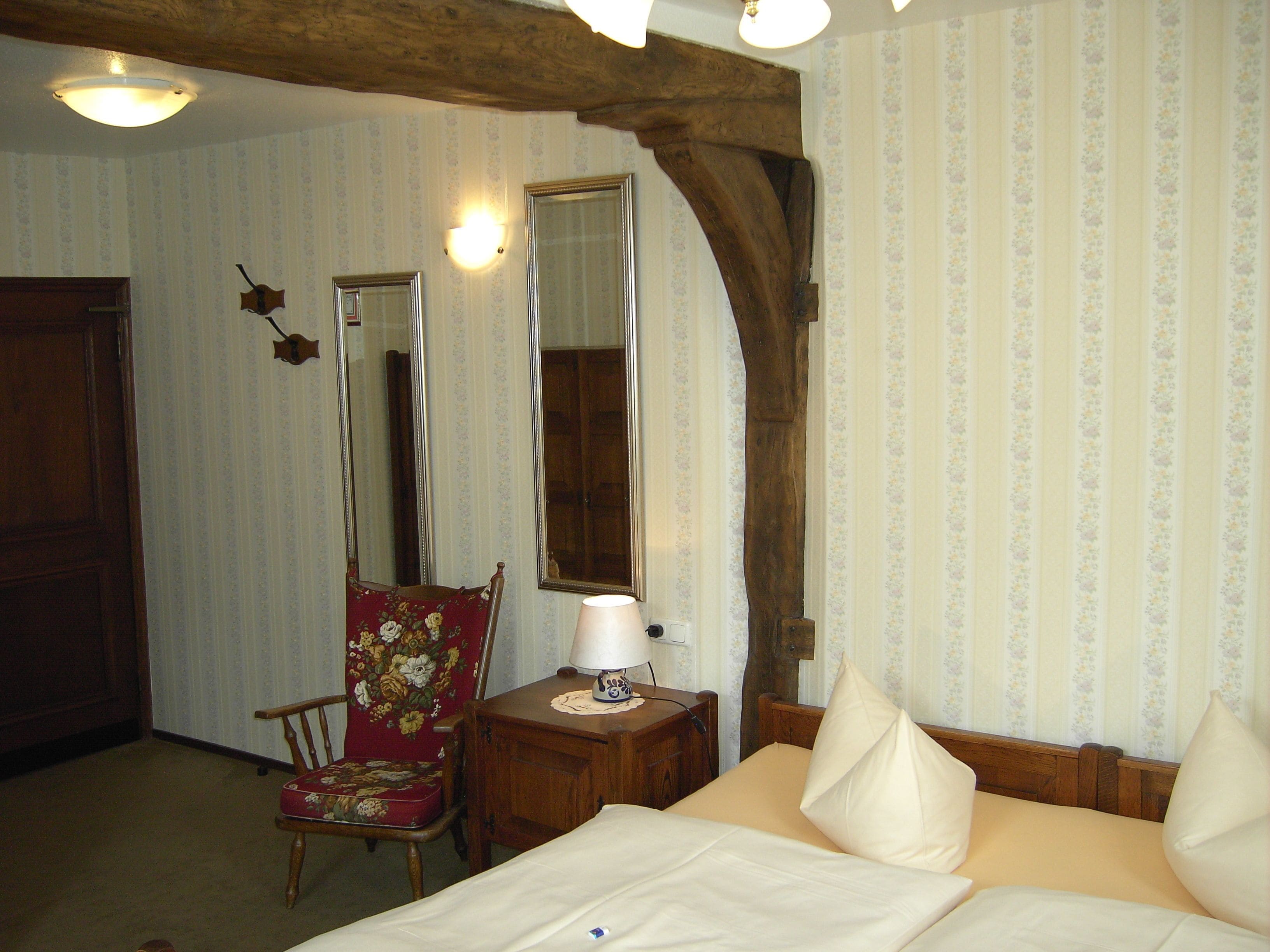 Ein Zimmer mit einem Bett, einem Sessel, einem Nachttisch und einem Spiegel.