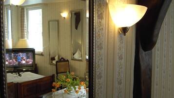 Une chambre avec un lit, une table de chevet ornée d’un vase de fleurs, une télévision et un miroir.