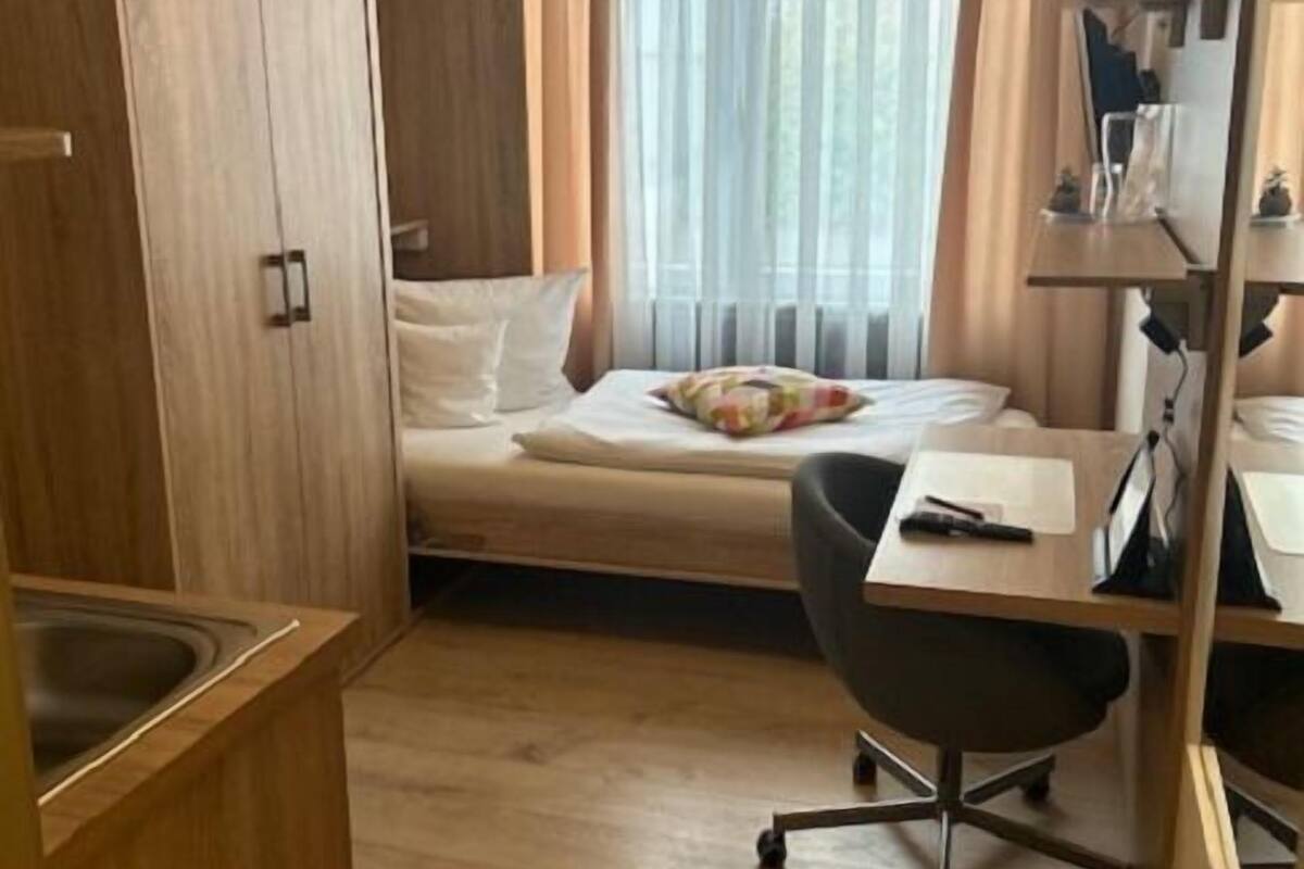 A compact hotel room with a bed, a desk, and a kitchenette area.