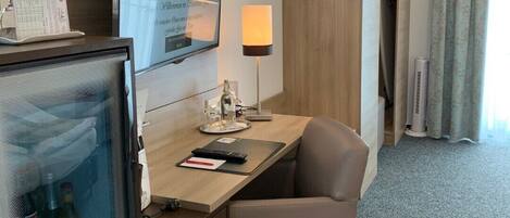 Une chambre d’hôtel équipée d’un bureau, d’une chaise, d’une télévision, d’une lampe et d’un mini-bar.