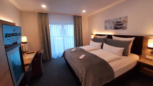 A hotel room with a large bed, a desk with a computer, and a television on the left. - Stadthotel Geis (Bad Neustadt an der Saale)