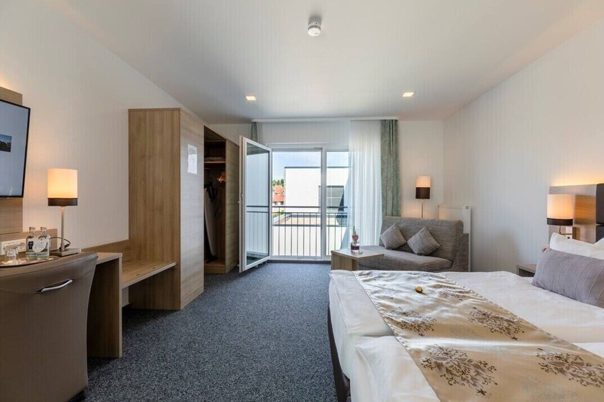 A hotel room with a bed, a desk, a chair, a small table, and a balcony with a view.