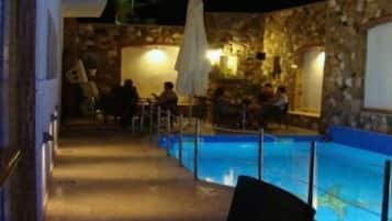 An outdoor pool area with stone walls, a few people sitting and relaxing, and a covered seating area.