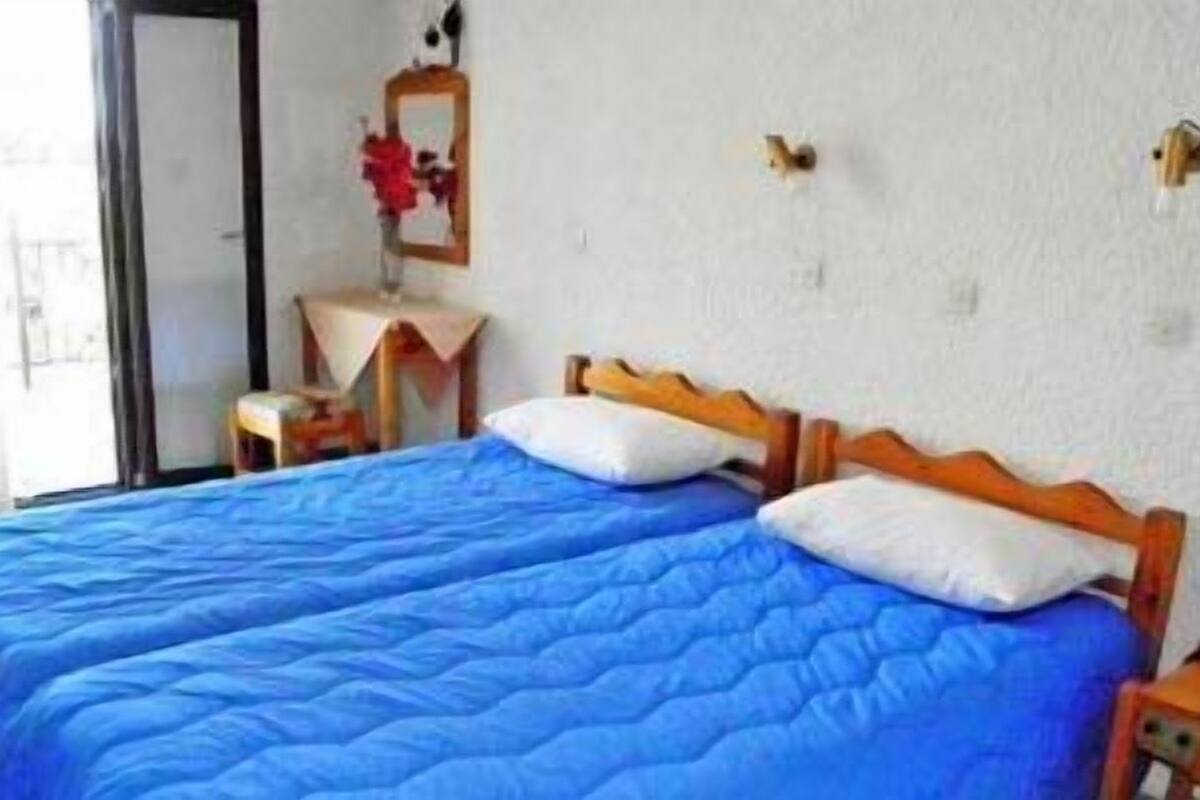 A double bed with blue bedding, a bedside table, a mirror, and a wall-mounted light fixture.