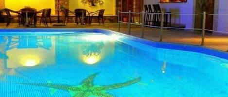 A swimming pool with a starfish decoration, surrounded by chairs and tables, and a wall with a chandelier.