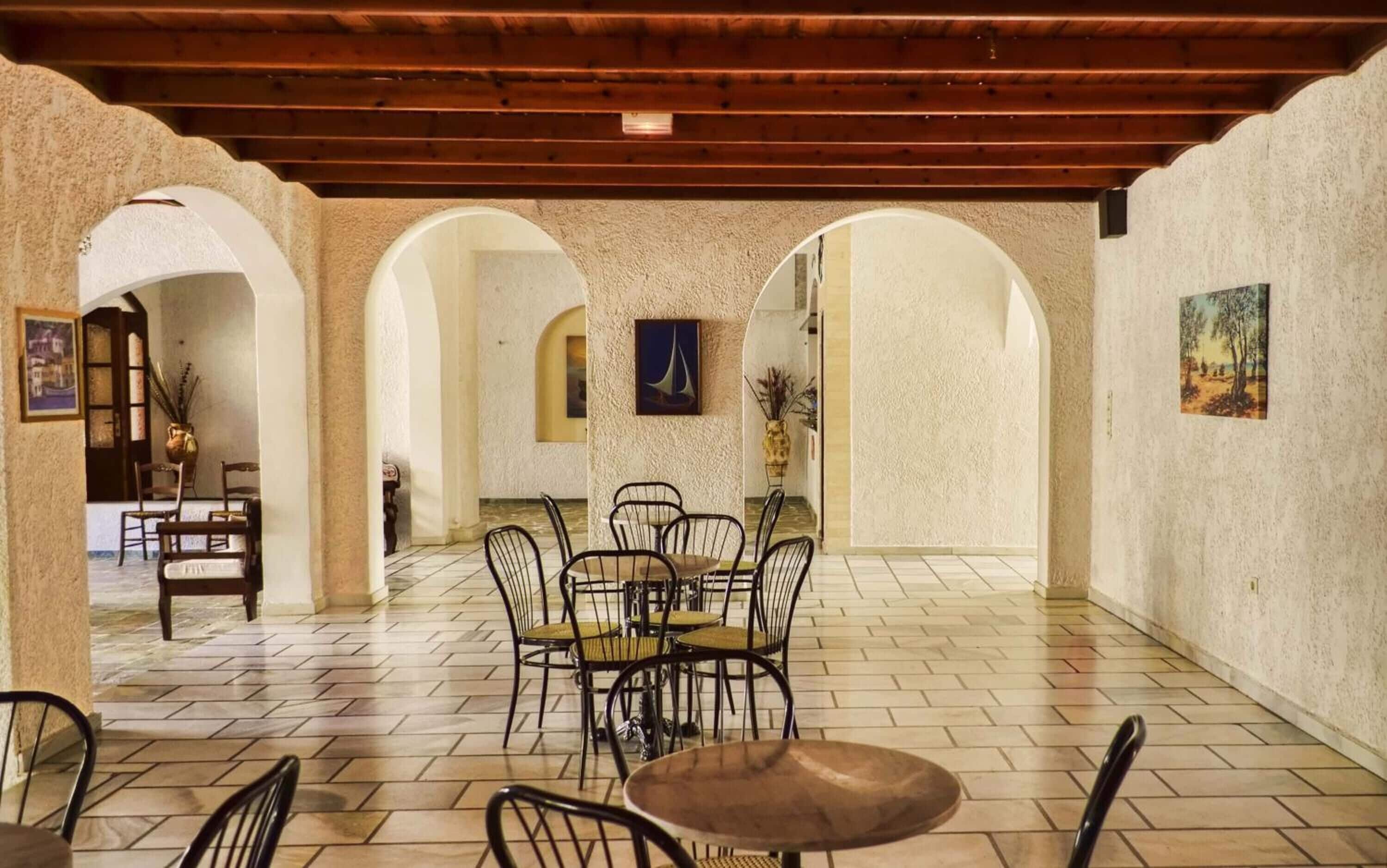 A spacious interior with a tiled floor, wooden ceiling beams, and a central dining area with chairs and a table.