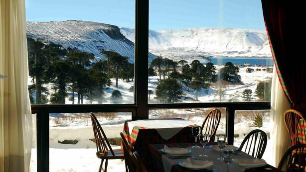 A dining area with a table set for two, overlooking a snowy landscape with trees and mountains. - Farallon (CAVIAHUE)