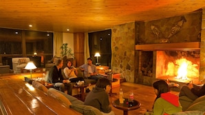 A cozy lounge area with a stone fireplace, wooden furniture, and a large window. - Farallon (CAVIAHUE)