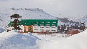 A multi-story building with a green roof, surrounded by snow-covered landscape and trees. - Farallon (CAVIAHUE)