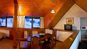 A cozy attic bedroom with wooden beams, a bed, a desk, and a television. - Farallon (CAVIAHUE)