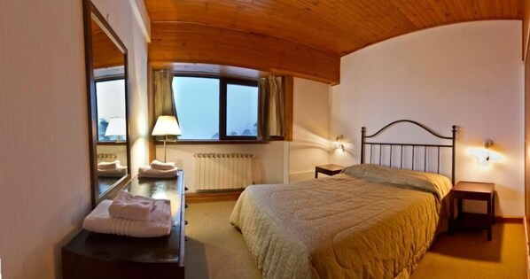 A bedroom with a bed, a bedside table, a lamp, a mirror, and a window with curtains. - Farallon (CAVIAHUE)