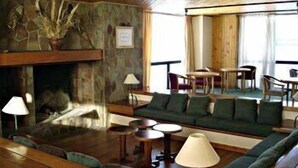 A cozy living room with a stone fireplace, green sofa, wooden floors, and a dining area with a table and chairs. - Farallon (CAVIAHUE)