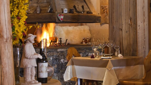 A rustic dining area with a stone fireplace, wooden beams, and a table set for two with wine glasses and a bottle. - Le Sherpa (Les Belleville)