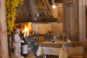 A rustic dining area with a stone fireplace, wooden beams, and a table set for two with wine glasses and a bottle. - Le Sherpa (Les Belleville)