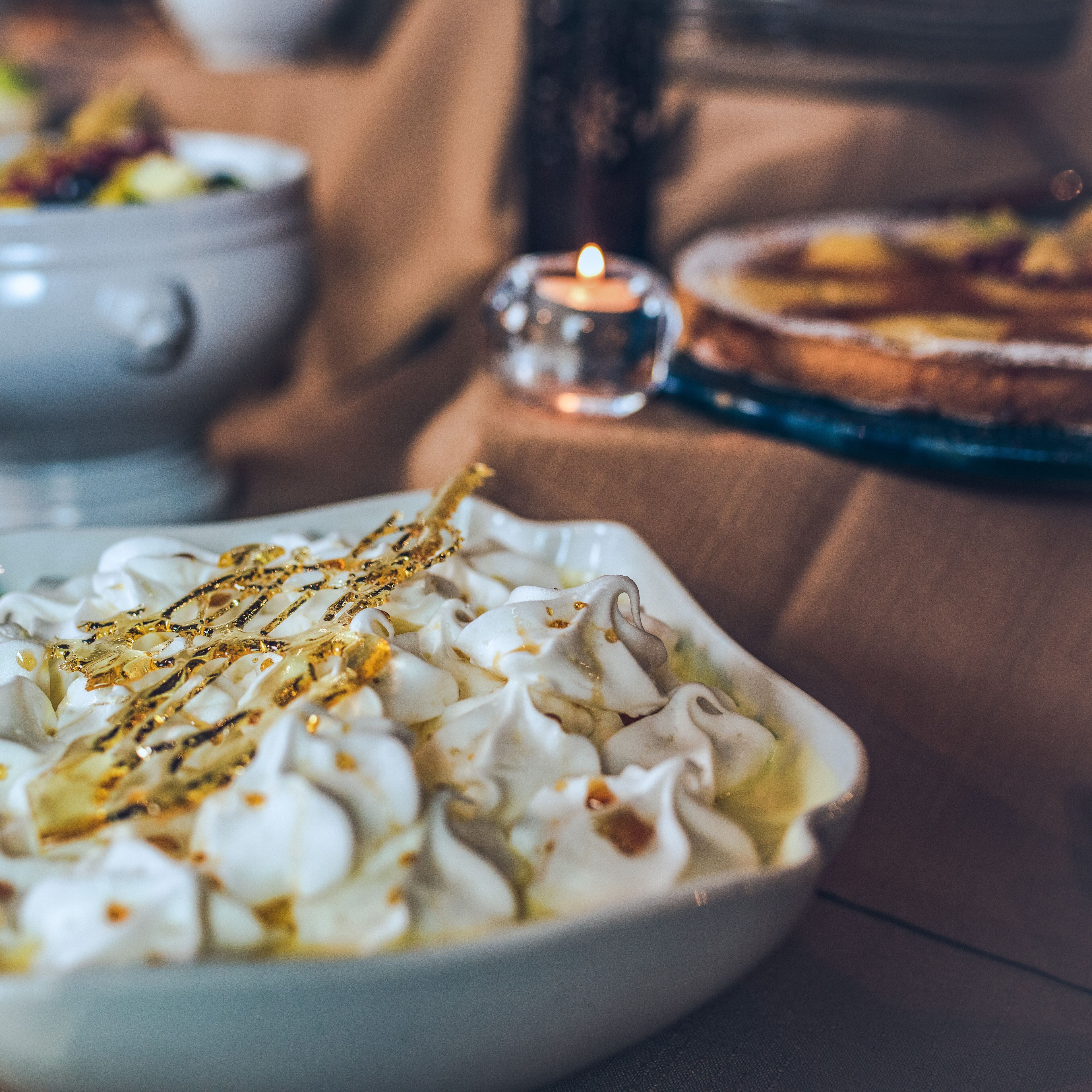 Un postre con crema batida y un chorrito dorado, sobre una mesa con una vela al fondo.