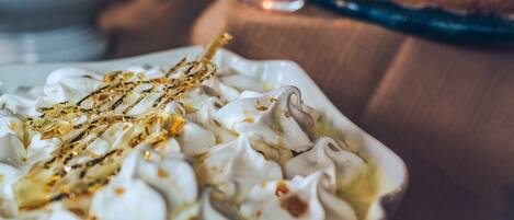 Un postre con crema batida y un chorrito dorado, sobre una mesa con una vela al fondo.
