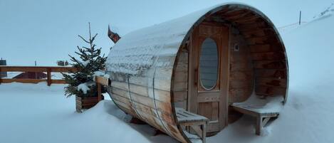 A snow-covered wooden cabin with a door and a bench outside.