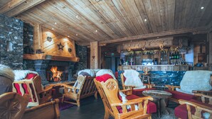 A cozy lodge interior with wooden furniture, a stone wall, a fireplace, and a bar area. - Le Sherpa (Les Belleville)