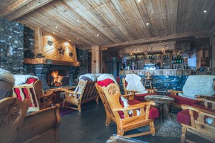 En mysig stuga med träinredning, en vägg av sten, en öppen spis och en bar.